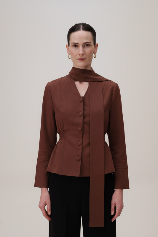 Woman wearing a brown blazer with a high collar against a plain background