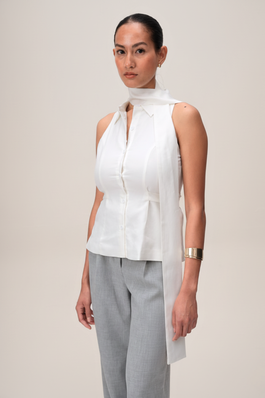 Woman wearing a white sleeveless blouse with a high collar and gray pants on a plain background