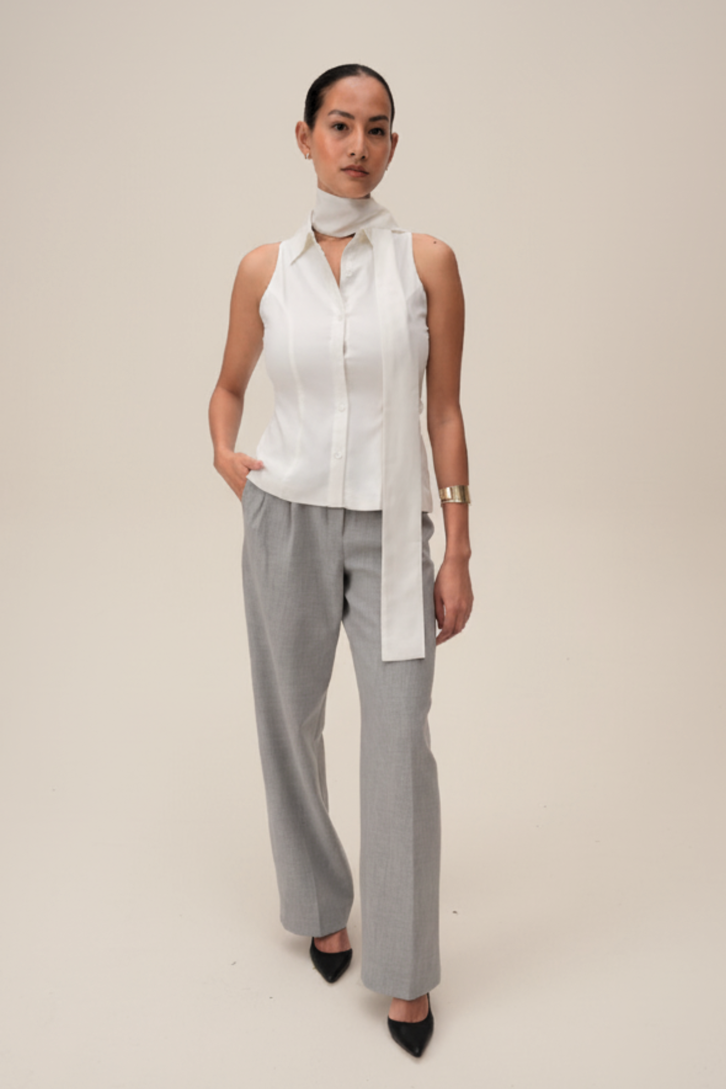 Woman wearing a white sleeveless top and gray pants on a beige background