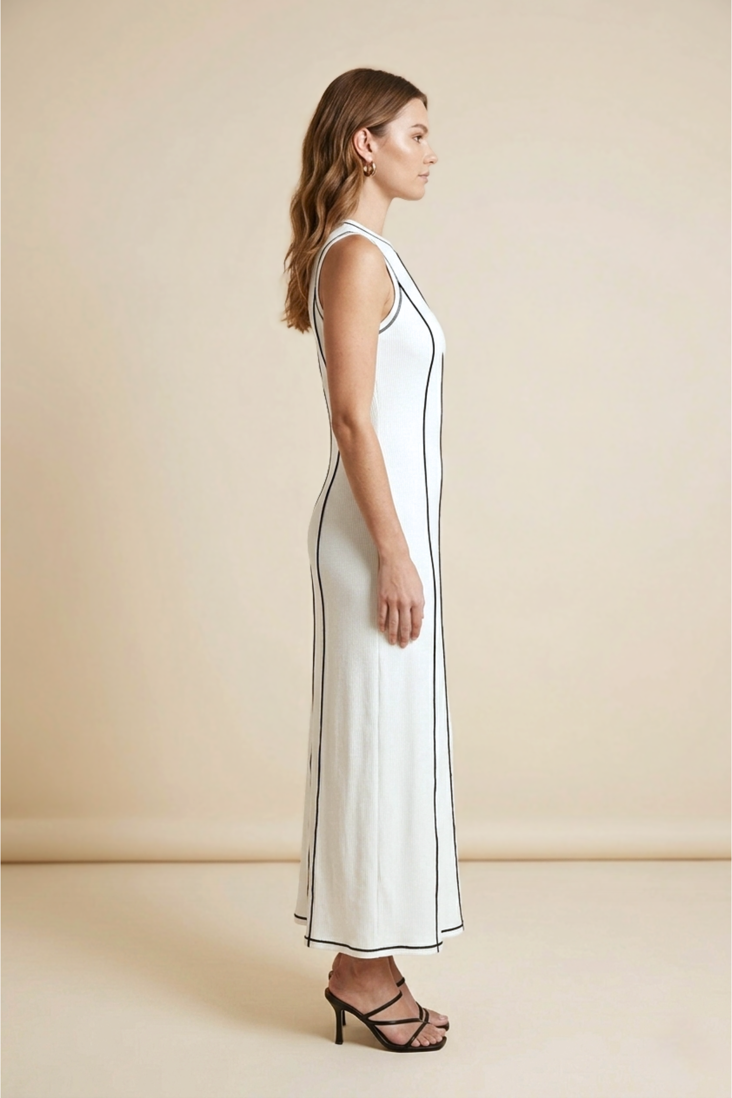 Woman wearing a white sleeveless dress with black trim on a beige background